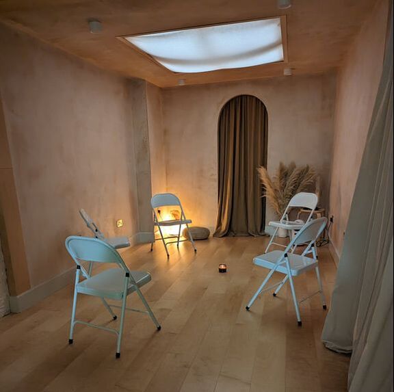 Downstairs space at Native self, soft pink walls, gentle lighting and a circle of plain white chairs